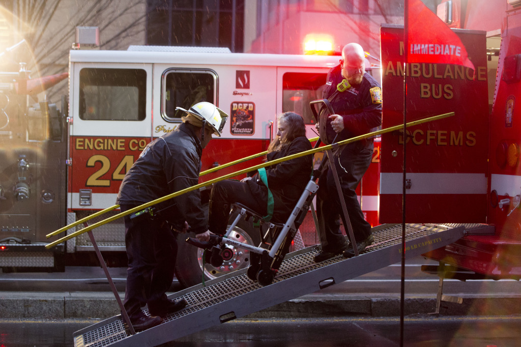 A woman is transported in a wheelchair onto an ambulance bus as people are evacuated from a smoke filled Metro subway tunnel in Washington, Monday, Jan. 12, 2015. Metro officials say one of the busiest stations in downtown Washington has been evacuated because of smoke.  Authorities say the source of the smoke is unknown. (AP Photo/Jacquelyn Martin)
