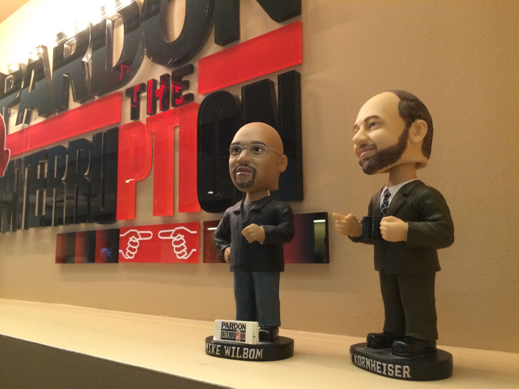Bobbleheads of the hosts stand in front of the logo in PTI's D.C. offices. (WTOP/Noah Frank)