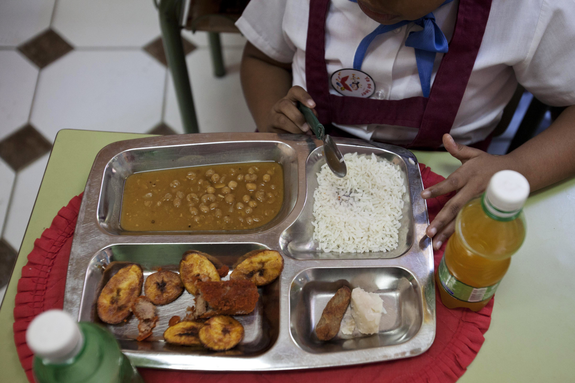 Milagro Ramos, a student at the Angela Landa elementary school, spoons up rice from her lunch tray, which also contains a chicken croquette, a piece of taro root and yellow pea soup in Old Havana, Cuba, Tuesday, May 6, 2014. Milagro brought fried plantains, lower left corner of her tray, and an orange drink from home. The children provide their own drinks. (AP Photo/Franklin Reyes)