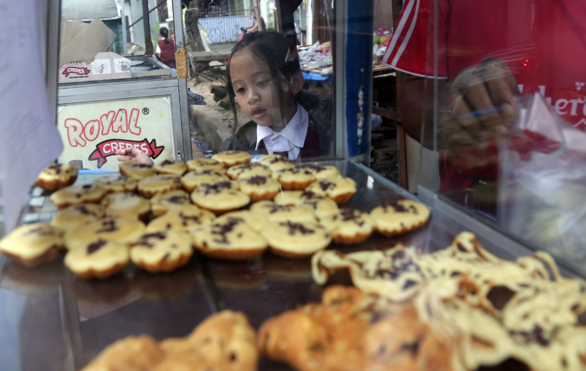 A public elementary school girl buys a pancake for her lunch on the street in Jakarta, Indonesia, Tuesday, May 6, 2014. In Indonesia, not every student can bring a lunch box to school. Public school students buy their lunch at school cafeterias or food stalls on the nearby streets. The price for one pancake is about one U.S. cent. (AP Photo/Achmad Ibrahim)