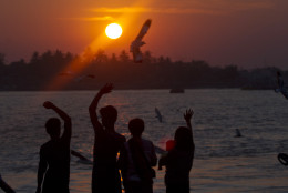 A group of people wave as seagulls fly near by during the last sun set of the year at a jetty in Yangon river, Myanmar, Wednesday, Dec.31, 2014. (AP Photo/Khin Maung Win)