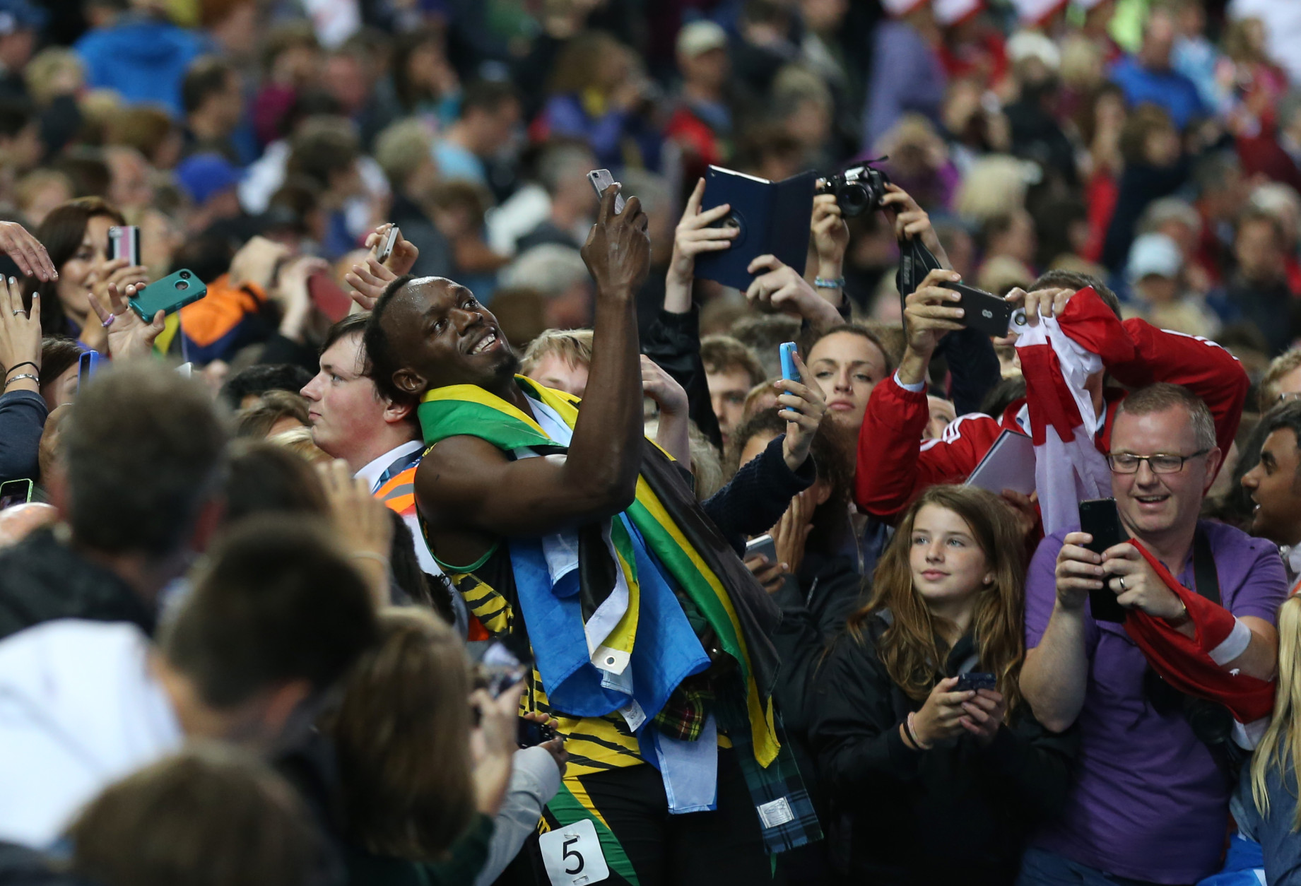 FOR USE AS DESIRED, YEAR END PHOTOS - FILE - Usain Bolt of Jamaica takes a photo on a smart phone with a member of the crowd as he walks round Hampden Park Stadium after he competed in the men's 4x100 meter relay race during the Commonwealth Games 2014 in Glasgow, Scotland, Saturday Aug. 2, 2014. (AP Photo/ Scott Heppell, File)