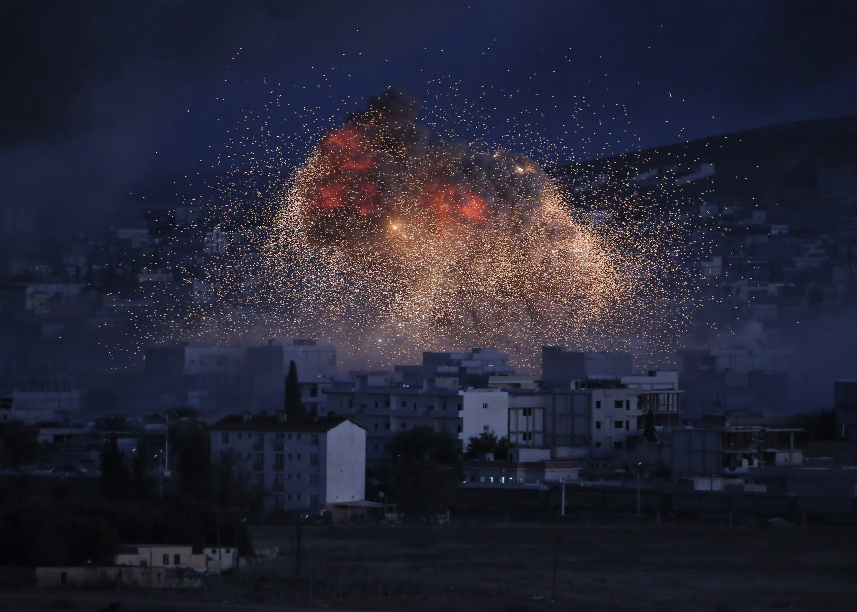 FOR USE AS DESIRED, YEAR END PHOTOS - FILE - Thick smoke and flames from an airstrike by the U.S.-led coalition rise in Kobani, Syria, as seen from a hilltop on the outskirts of Suruc, at the Turkey-Syria border, Monday, Oct. 20, 2014. Kobani, also known as Ayn Arab, and its surrounding areas, has been under assault by extremists of the Islamic State group since mid-September and is being defended by Kurdish fighters. (AP Photo/Lefteris Pitarakis, File)