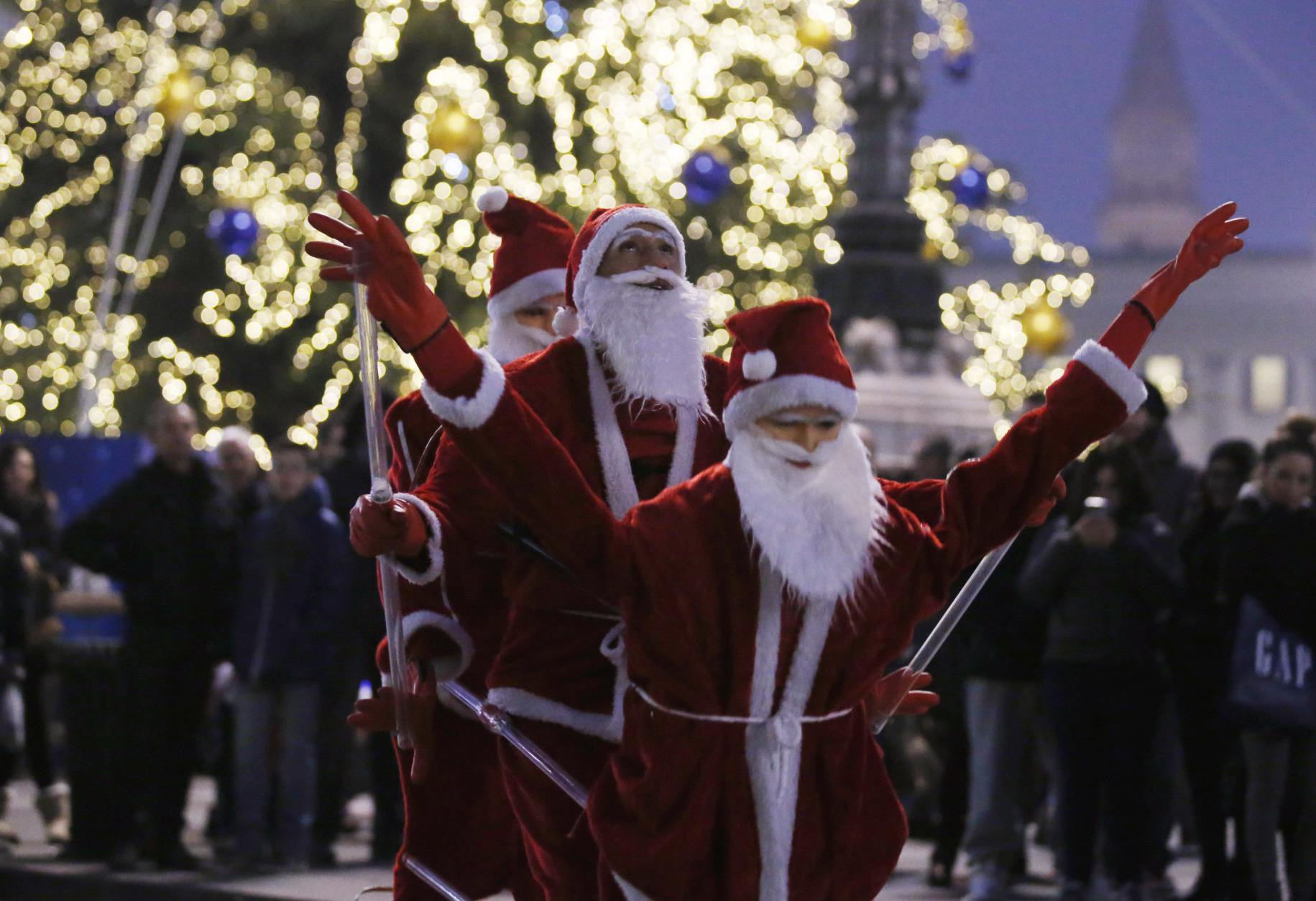 A street artist performs dressed as Santa Klaus with two life-size puppets in Milan, Italy, Saturday, Dec. 20, 2014. (AP Photo/Luca Bruno)