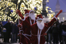 A street artist performs dressed as Santa Klaus with two life-size puppets in Milan, Italy, Saturday, Dec. 20, 2014. (AP Photo/Luca Bruno)