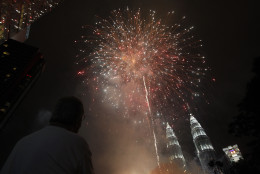 A man watches fireworks explode over Malaysia's landmark Petronas Twin Towers during New Year celebrations in Kuala Lumpur, Malaysia, Thursday, Jan. 1, 2015. (AP Photo/Lai Seng Sin)