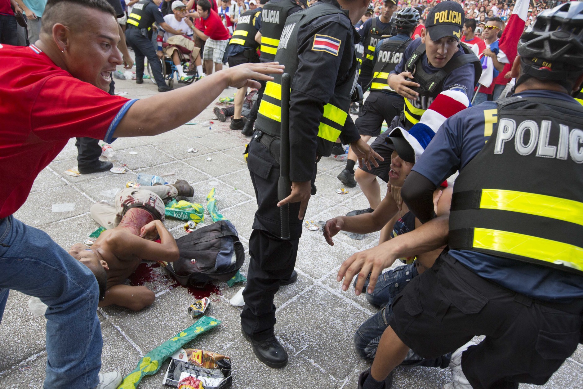 FOR USE AS DESIRED, YEAR END PHOTOS - FILE - A Costa Rica soccer fan is detained by the police while another fan lies on the ground injured with a knife, after a fight broke out during the live telecast of the quarterfinal World Cup match between Costa Rica and The Netherlands, at Democracy square in San Jose, Costa Rica, Saturday, July 5, 2014. Dutch Goalie Tim Krul came on as a substitute in the final minute of extra time and then saved two penalties in a 4-3 shootout victory over Costa Rica on Saturday, giving the Netherlands a spot in the World Cup semifinals. (AP Photo/Esteban Felix, File)