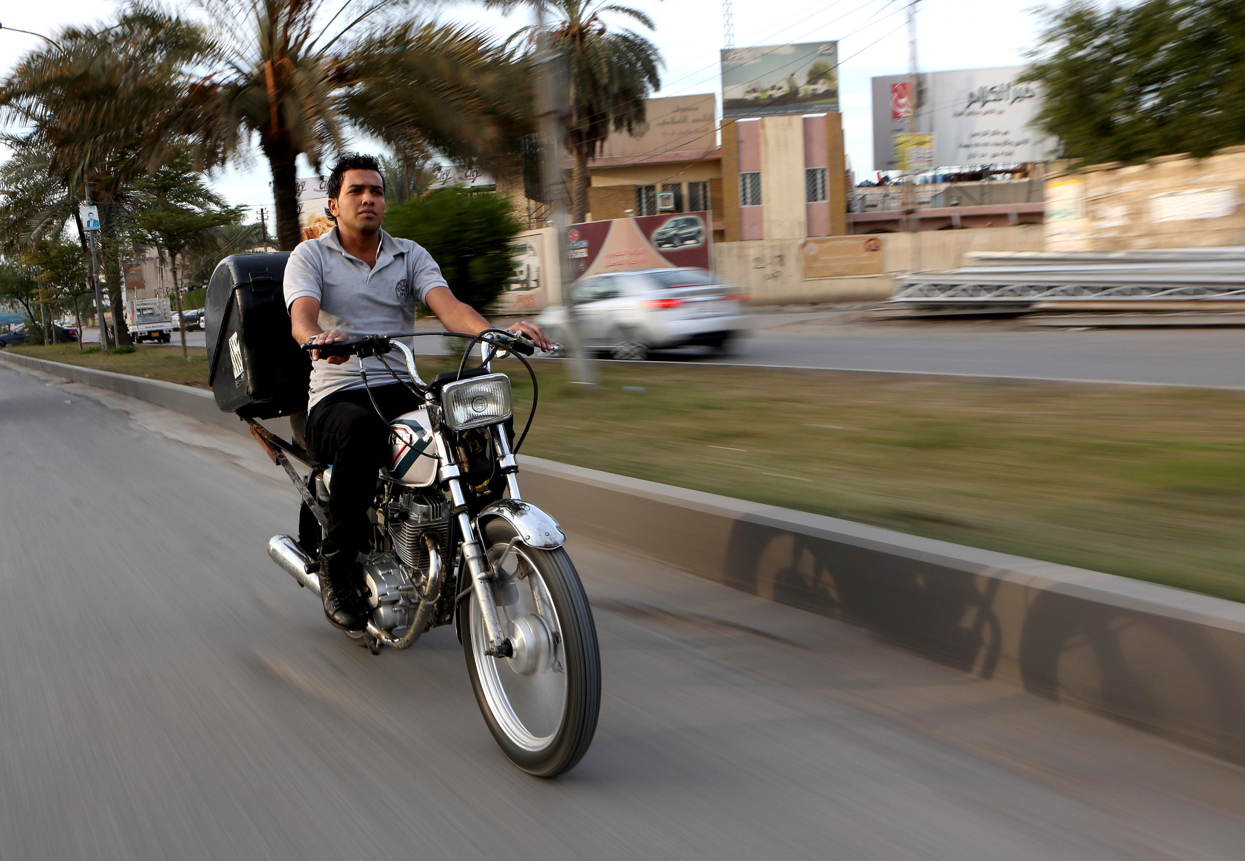 In this Sunday, Nov. 30, 2014 photo,  22-year-old Hassan Khudair, makes his way on a motorbike to deliver food, in Baghdad, Iraq. As he rushes pizza and shwarma sandwiches to waiting customers, Khudier has to deal with the countless security checkpoints in the Iraqi capital and the risk of being in the wrong place at the wrong time in a city where car bombings and suicide blasts take place nearly daily. (AP Photo/Hadi Mizban)