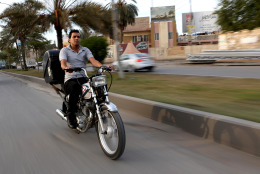 In this Sunday, Nov. 30, 2014 photo,  22-year-old Hassan Khudair, makes his way on a motorbike to deliver food, in Baghdad, Iraq. As he rushes pizza and shwarma sandwiches to waiting customers, Khudier has to deal with the countless security checkpoints in the Iraqi capital and the risk of being in the wrong place at the wrong time in a city where car bombings and suicide blasts take place nearly daily. (AP Photo/Hadi Mizban)