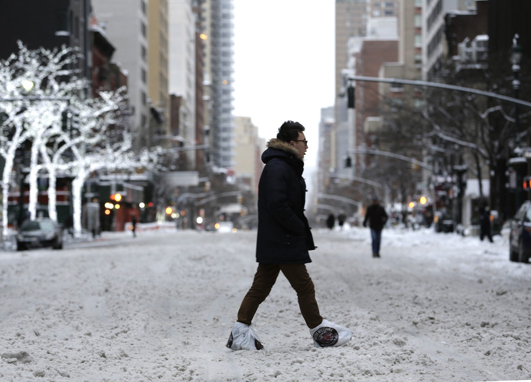 A man wearing plastic bags on his feet crosses a snowy avenue in New York, Tuesday, Jan. 27, 2015. A storm packing blizzard conditions spun up the East Coast early Tuesday, pounding parts of coastal New Jersey northward through Maine with high winds and heavy snow. (AP Photo/Seth Wenig)