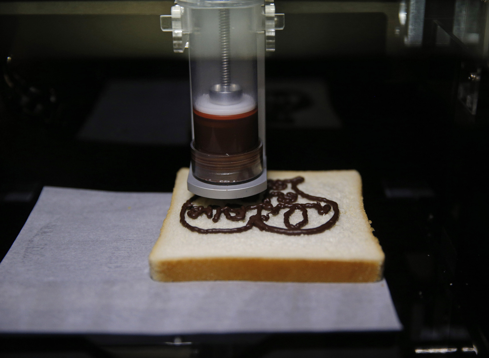 The XYZprinting 3D Food Printer displays a design in chocolate on a piece of bread at CES Unveiled, a media preview event for CES International, Sunday, Jan. 4, 2015, in Las Vegas. (AP Photo/John Locher)