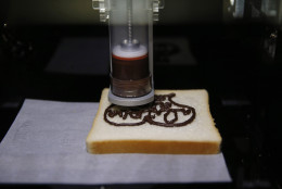 The XYZprinting 3D Food Printer displays a design in chocolate on a piece of bread at CES Unveiled, a media preview event for CES International, Sunday, Jan. 4, 2015, in Las Vegas. (AP Photo/John Locher)