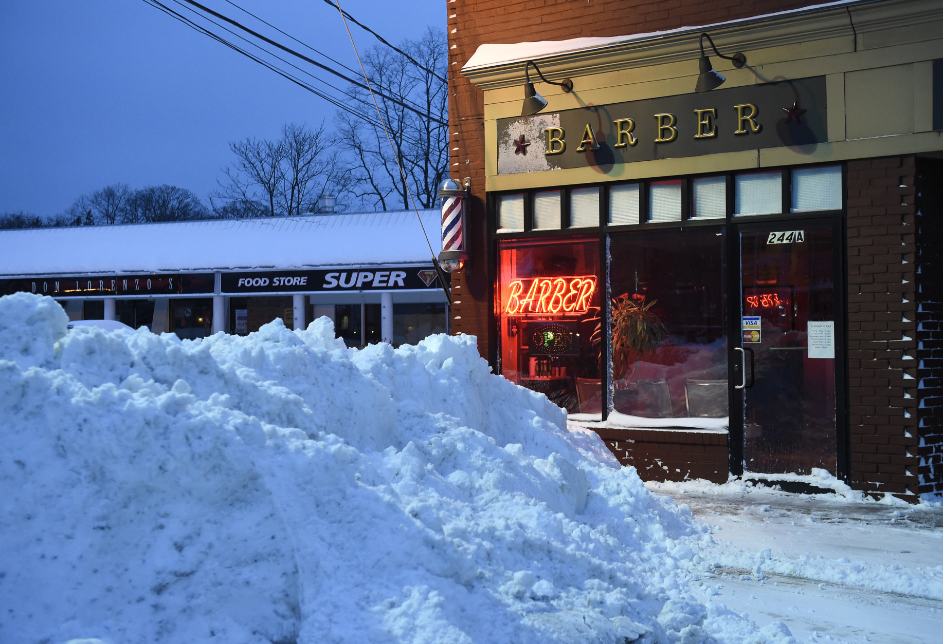 Snow from plows piles up in front of a barber shop on Glen Cove Avenue on Tuesday, Jan. 27, 2015, in  Glen Cove, N.Y.  A storm packing blizzard conditions spun up the East Coast early Tuesday, pounding coastal eastern Long Island into Maine with high winds and heavy snow. (AP Photo/Kathy Kmonicek)