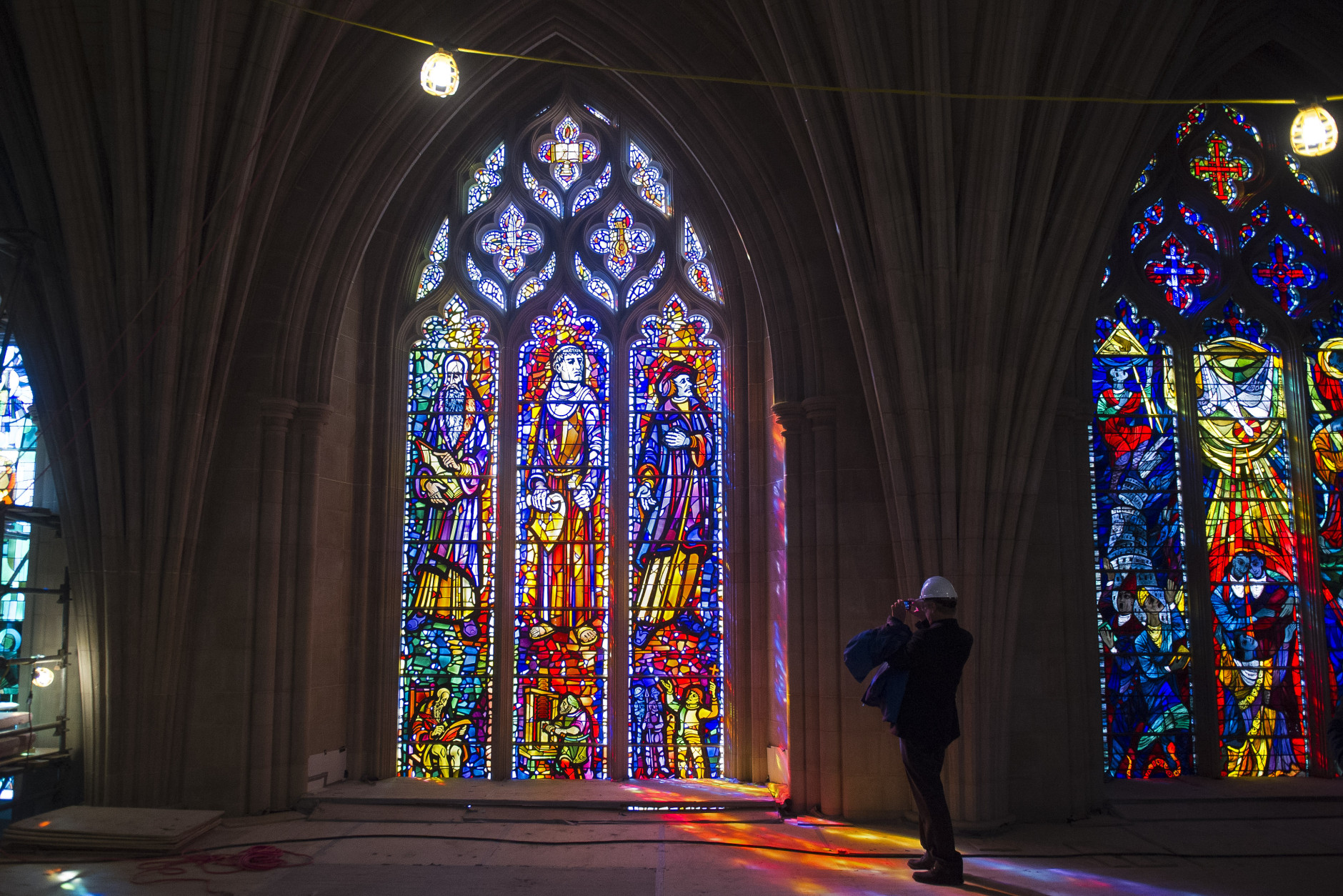 A reporter, standing on a scaffold platform 65 feet above the nave floor, takes a photograph of a recently cleaned and repaired stained glass window at  the Washington National Cathedral in Washington, Wednesday, Feb. 18, 2015. This marks the completion of the first phase in the building's $32 million restoration effort. (AP Photo/Cliff Owen)