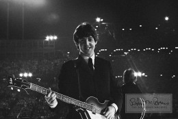 In a beautifully intimate moment in the middle of 25,000 fans, Paul McCartney turns away from the audience and beams when he finds Bob Bonis. The Bloomington, Minnesota, show on August 21, 1965, was the Beatles’ only stop in the Land of 10,000 Lakes on all three US tours. Though it was one of the few shows on the 1965 tour that didn’t sell out, for the then-bargain price of $2.50 to $5.50 per ticket (about $20-40 today), fans sang along with: She’s A Woman, I Feel Fine, Dizzy Miss Lizzy, Ticket to Ride, Everybody’s Trying To Be My Baby, Can’t Buy Me Love, Baby’s In Black, I Wanna Be Your Man, A Hard Day’s Night, Help! and I’m Down. Because of a security breach at the airport promoter Ray “Big Reggie” Colihan declared that no journalists, or photographers, not even the Mayor of Bloomington would be permitted on the field.   So Bonis’ photographs, who as tour manager stood at the side of the stage, are the only close-up shots taken that night. And the Beatles’ genuine affection for their tour manager and friend is lovingly captured here.
