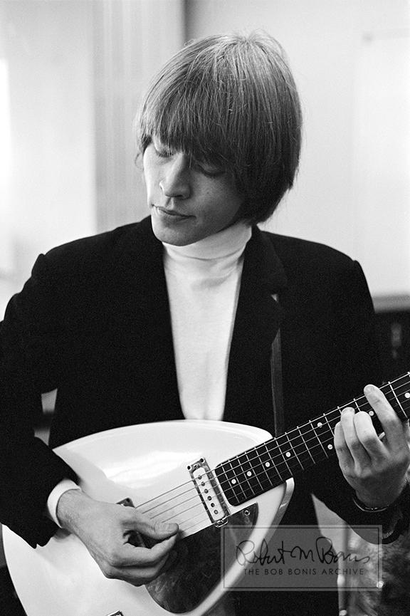 This unassuming portrait shows Rolling Stones’ founding member Brian Jones at a rehearsal for the T.A.M.I. Show, caught up in a melody as he strums his 1964 Vox MK III “Teardrop” guitar. The one-of-a-kind prototype guitar was custom-made for Brian by Vox. Though he played it onstage frequently during the Stones’ 1964 and 1965 tours, Brian did not use it as often in the studio, because it had an odd shape and was difficult to play while sitting. In the beginning, Brian and Keith Richards rarely shared guitars (later they would become way more communal). Forever linked to Brian’s unique legacy, this stunning guitar is one of the most famous Rolling Stones instruments of all time.