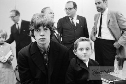 A few days into their second US tour, Mick Jagger obliges a young fan with a backstage photo op during the taping of the T.A.M.I. Show “filmed in Electronovision” (video transferred to film) at the Santa Monica Civic Auditorium in Santa Monica, California. The unique concert film stood for either “Teenage Awards Music International,” or “Teen Age Music International” depending on which piece of publicity you read and was released in theaters on December 29, 1964. The show’s music director, Jack Nitzsche, often hung with the Stones, and even played piano (and the mythical “nitzschephone” coined by manager-producer Andrew Loog Oldham) on many of their RCA sessions, from Aftermath to Sticky Fingers. The Rolling Stones followed James Brown & The Famous Flames in the lineup, who declared at the time “I’m gonna make the Rolling stones wish they’d never come to America.”   In fact the future Godfather of Soul was so impressed by their performance that he congratulated them as they came off the stage and invited them to come see him perform at the Apollo a few weeks later.  The boy in the photo is most likely the son of one of the VIPs in attendance, as the Stones were often called upon for forced photo ops at the bequest of big-shot record label executives and other VIPs.