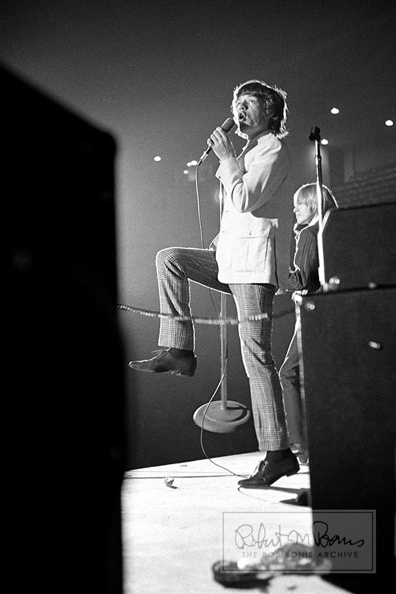 Mick Jagger sings his heart out for a totally hidden audience, as seen through the amps from tour manager Bob Bonis’ unique perspective from the side of the stage.  Original Rolling Stones founding member / guitarist Brian Jones can be seen beside him on the stage.  In an interview with Time, Mick admitted to stealing James Brown’s dance moves (and others’ moves, too) after meeting him when they filmed the T.A.M.I. Show movie more than 50 years ago. But it was more than just the moves, it was an attitude—an attitude that’s radiating from Mick in this photo.