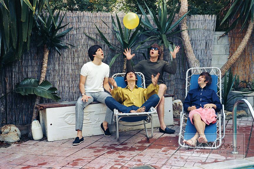 In a captivating moment of total playfulness, all four Beatles - Paul McCartney, John Lennon, George Harrison and Ringo Starr - are photographed on vacation in Bel Air, California on August 23-24, 1964. With such an intense schedule, downtime was a luxury, yet this mini-vacation almost didn’t happen. In town for their August 23 historic show at the famous Hollywood Bowl, the boys soon found out that L.A. wasn’t exactly willing to roll out the red carpet. Lockheed Airport in Burbank refused to let their plane land, and The Ambassador Hotel cancelled their reservations out of fear of being inundated with crazed fans. Luckily, British actor Reginald Owen offered up his Bel Air manse for the bargain price of $1,000. While in town, the Beatles hit up the iconic Whisky A Go Go club with Jane Mansfield, where George Harrison infamously threw a drink at the paparazzi, but hit Mamie Van Doren instead. They also met Burt Lancaster, with Ringo Starr dressed like a cowboy wielding toy guns that were reportedly gifts from Elvis Presley. Upon seeing Ringo, Burt quipped, “What have you got there? Kids’ stuff!” He later sent Ringo two real guns and a holster, which Ringo loved: “I just wanted to be a cowboy.” This photo captures four boys who just wanted to play - and the fact that both the late George Harrison and the late John Lennon have their arms outstretched, reaching skyward, is a really beautiful button.
