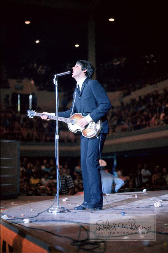 A serene crooning Paul McCartney is juxtaposed with a beyond-littered stage in this photo taken during an August 19, 1965, show at the Sam Houston Coliseum in Houston, Texas. The Beatles played two sold-out shows in Houston, advertised as the “Sixth Annual Back-to-School Show,” to capacity crowds of 9,200 screaming fans with general admission seating. Predominantly teenage girls suffering from Beatlemania (thanks to the recent release of the film HELP!), began tossing jellybeans on stage because George Harrison had mentioned he loved the softer (and totally unavailable) British version, jelly babies, in an interview. Along with a barrage of hard candy, fans threw paper, cups and even a few dangerous objects. Entertainment reporter Jeff Millar noted, “Nobody missed a note as cups caromed off their faces. George Harrison adroitly dodged the largest object hurled, apparently someone’s right tennis shoe.” But it was John Lennon who pithily summed up their second US tour so far: “We’ve only been to Dallas and here. And we almost got killed both places.” 
