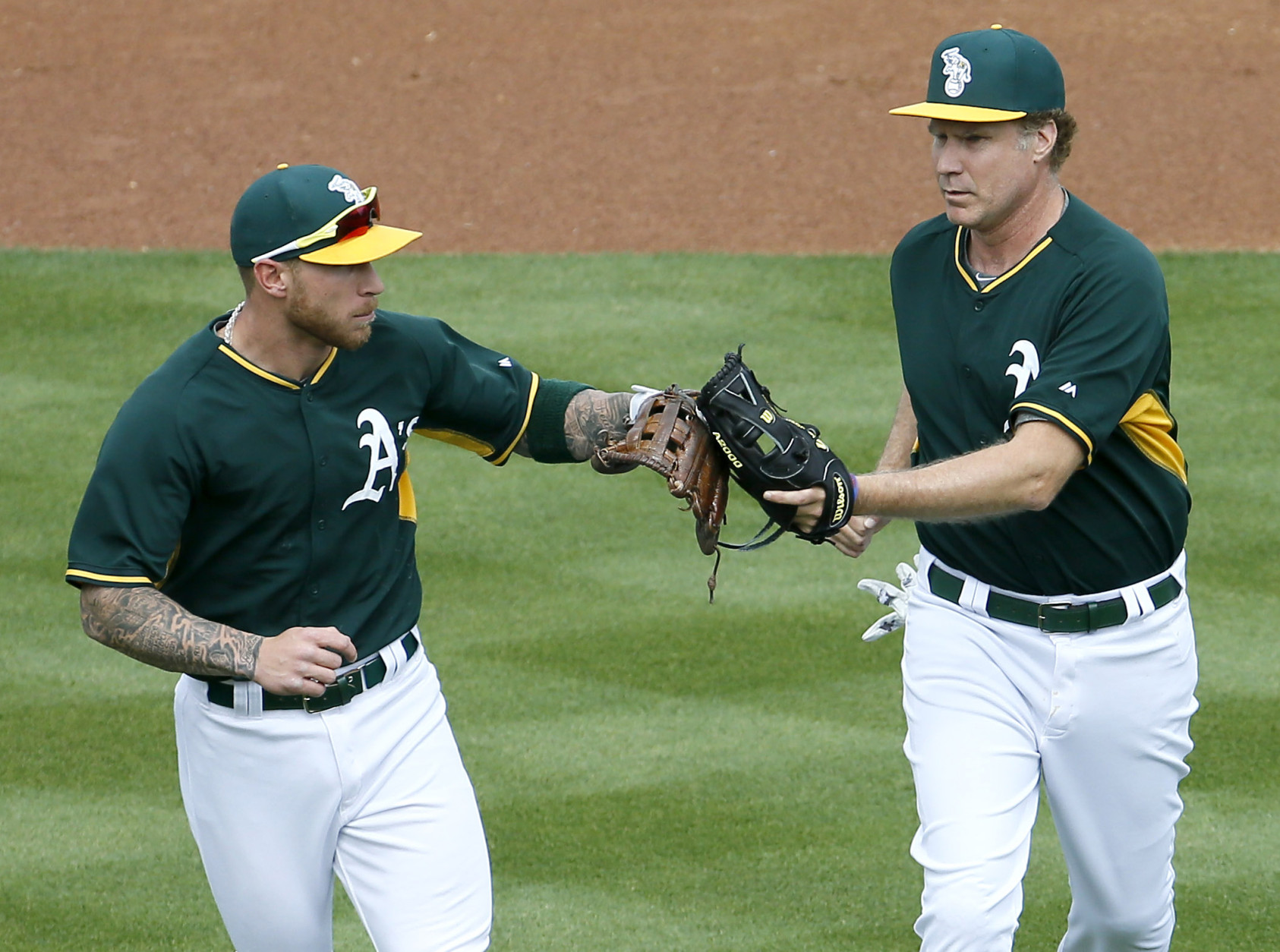Actor Will Ferrell, right, congratulates Oakland Athletics' Brett Lawrie after the first inning of a spring training baseball game against the Seattle Mariners, Thursday, March 12, 2015, in Mesa, Ariz. The comedian plans to play every position while making appearances at five Arizona spring training games on Thursday. (AP Photo/Matt York)