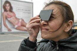 A woman uses tinted glass to watch a solar eclipse through a telescope outside a shopping mall in Bucharest, Romania, Friday, March 20, 2015. Clouds obscured the sun for most of the time the eclipse took place. (AP Photo/Vadim Ghirda)