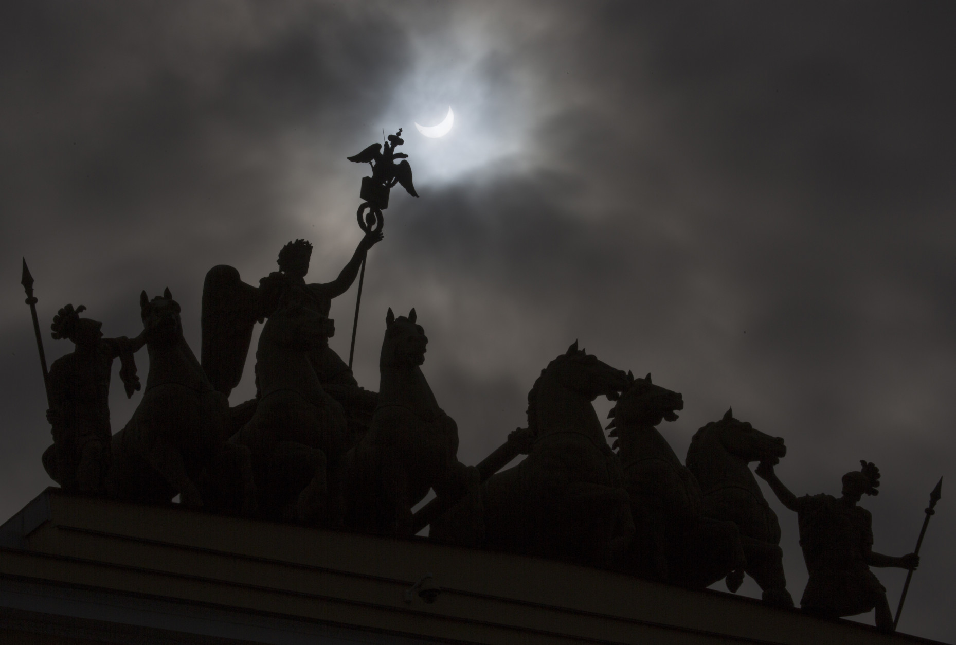 The moon blocks part of the sun during a solar eclipse as seen over a statue at the one of the city landmarks, the General Staff Headquarters in St.Petersburg, Russia, Friday, March 20, 2015. An eclipse is darkening parts of Europe on Friday in a rare solar event that won't be repeated for more than a decade.  (AP Photo/Dmitry Lovetsky)