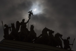 The moon blocks part of the sun during a solar eclipse as seen over a statue at the one of the city landmarks, the General Staff Headquarters in St.Petersburg, Russia, Friday, March 20, 2015. An eclipse is darkening parts of Europe on Friday in a rare solar event that won't be repeated for more than a decade.  (AP Photo/Dmitry Lovetsky)