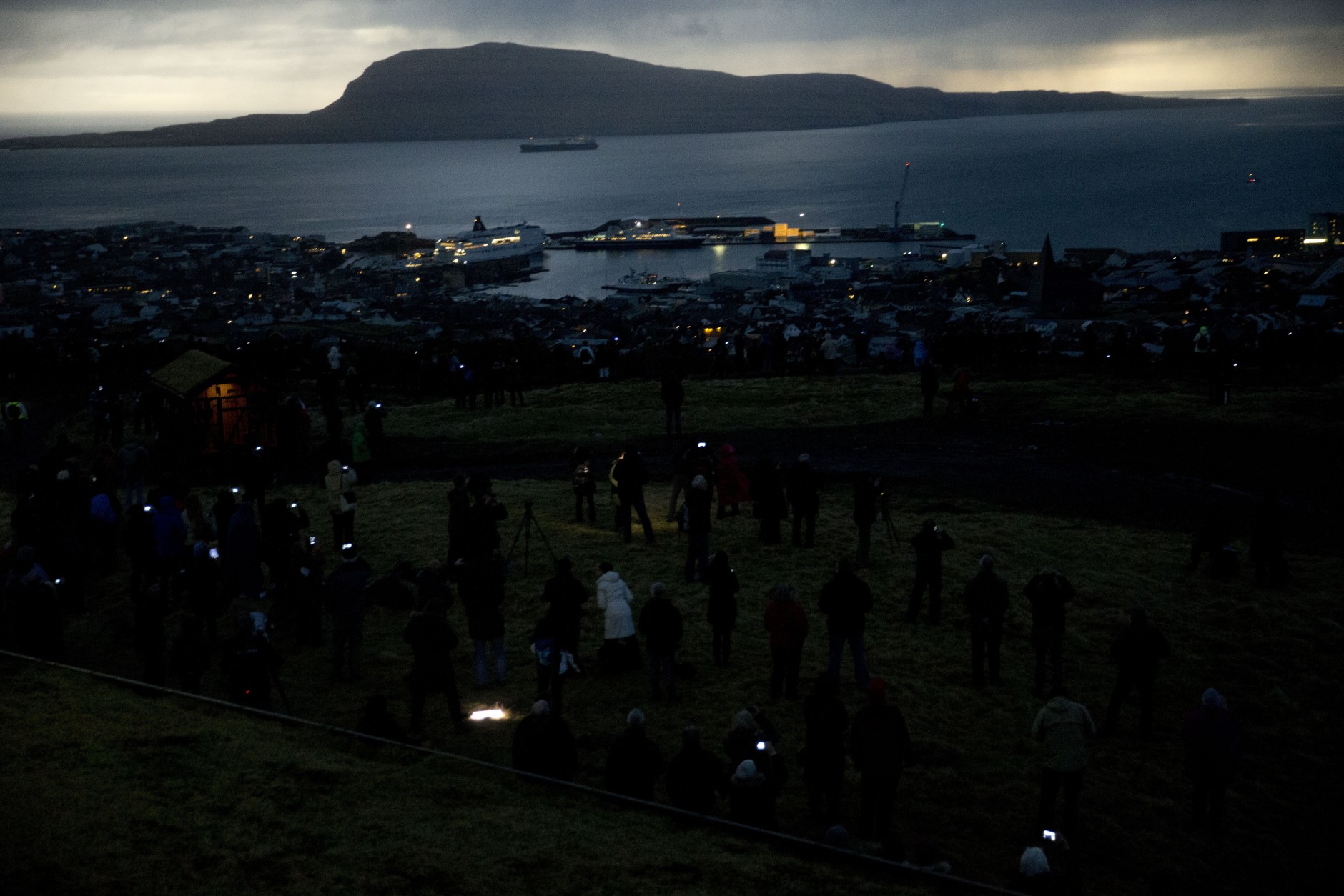 People watch in darkness during the totality of a solar eclipse on as seen from a hill beside a hotel on the edge of the city overlooking Torshavn, the capital city of the Faeroe Islands, Friday, March 20, 2015. For months, even years, accommodation on the remote Faeroe Islands has been booked out by fans who don't want to miss an almost three-minute-long astronomical sensation. Now they just have to hope the clouds will blow away so they can fully experience Friday's brief total solar eclipse.  (AP Photo/Matt Dunham)