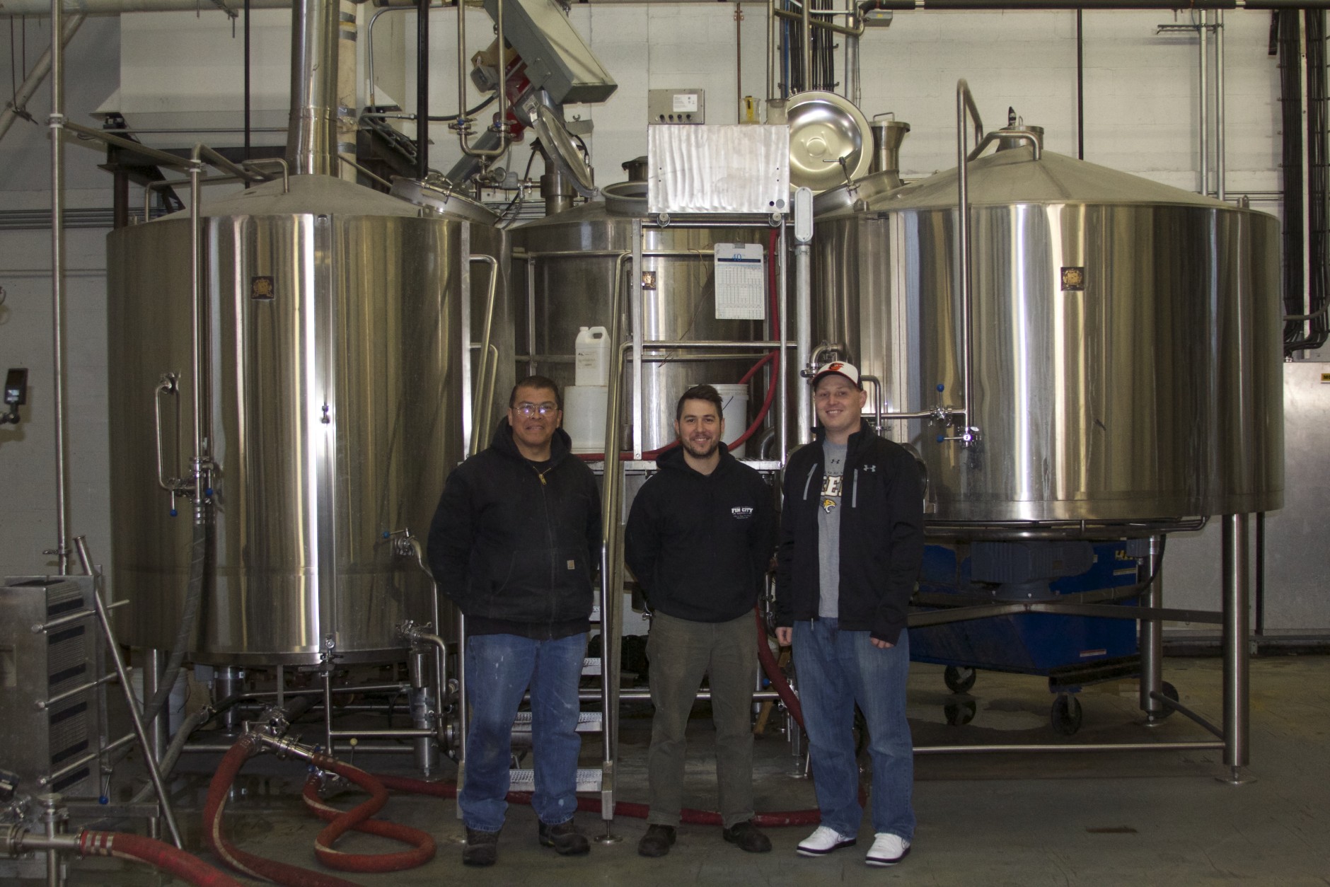 From left to right: Peabody Heights brewmaster Ernie L. Igot, brewer Eli Breitburg-Smith and co-owner Dan Baumiller stand in front of the machine responsible for distilling beer flavors before the beer enters its fermentation stage. 