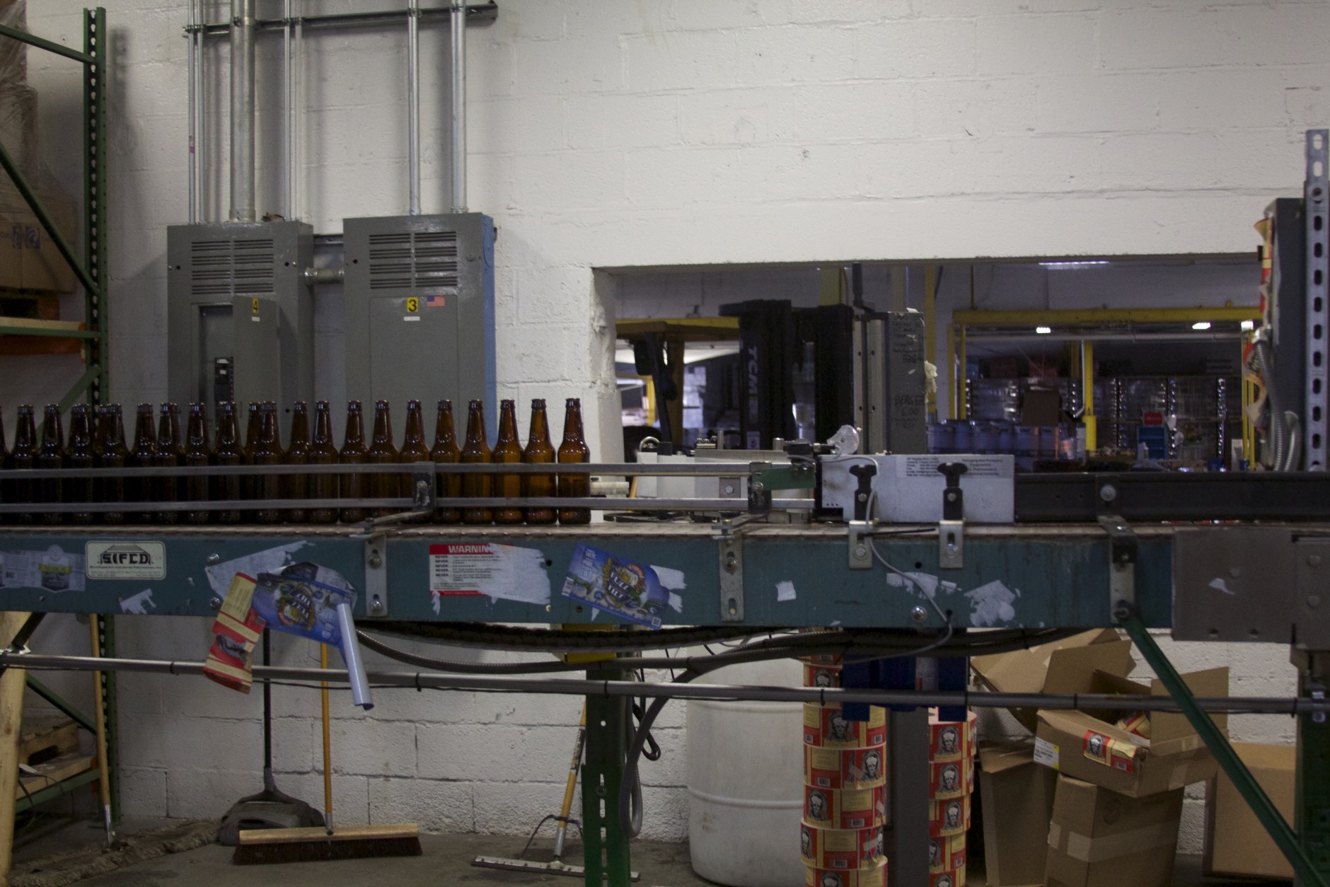 Empty bottles wait on a conveyor belt to be labeled, filled and packaged for sale. Full Tilt’s Bay IPA stickers hang off the machine’s side. 