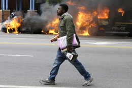 A man carries items from a store as police vehicles burn, Monday, April 27, 2015, after the funeral of Freddie Gray in Baltimore. Gray died from spinal injuries about a week after he was arrested and transported in a Baltimore Police Department van. (AP Photo/Patrick Semansky)
