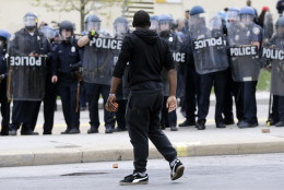 A demonstrator walks past police with a brick as they respond to thrown objects, Monday, April 27, 2015, after the funeral of Freddie Gray in Baltimore. Gray died from spinal injuries about a week after he was arrested and transported in a Baltimore Police Department van. (AP Photo/Patrick Semansky)