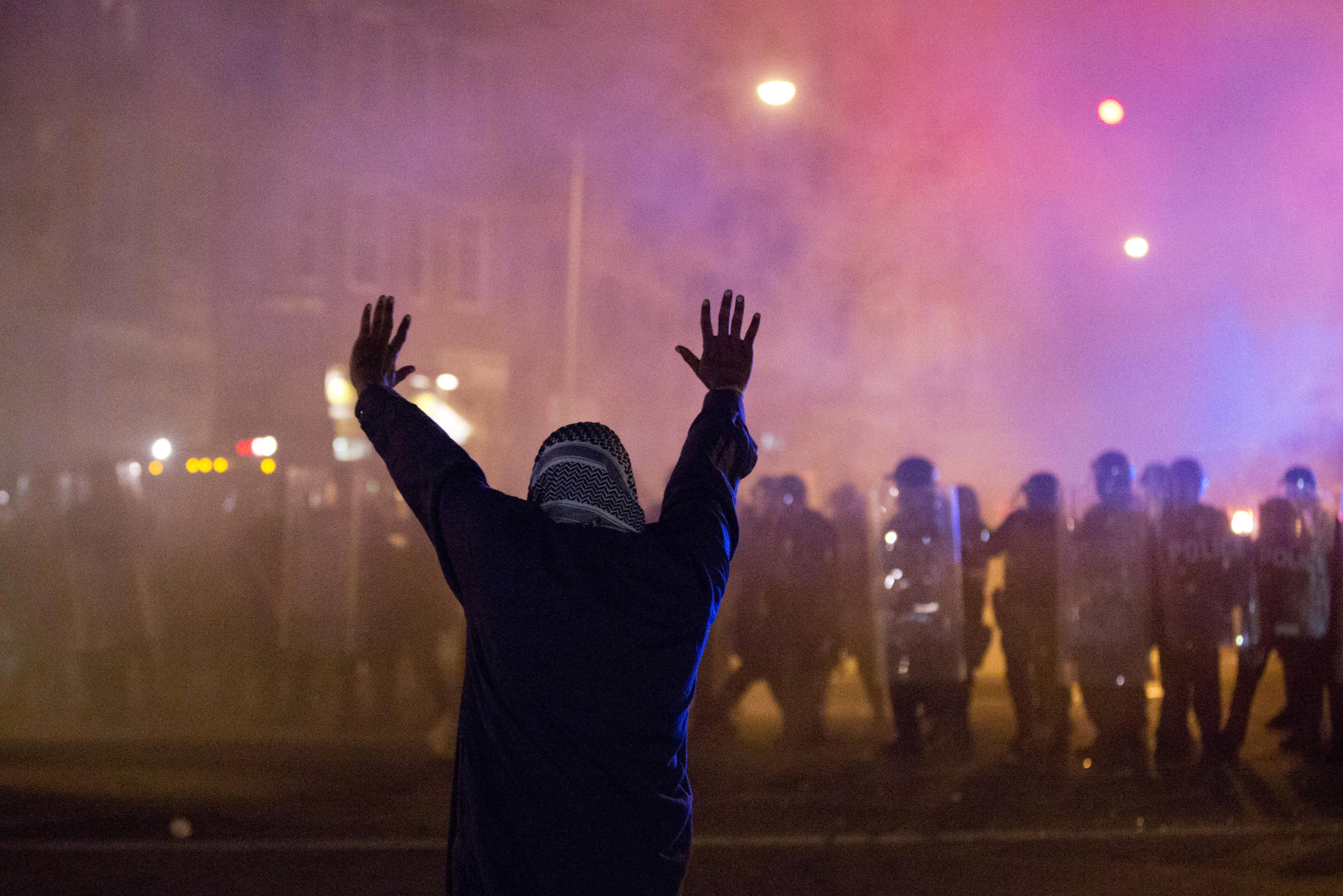A protestor faces police enforcing a curfew Tuesday, April 28, 2015, in Baltimore. A line of police behind riot shields hurled smoke grenades and fired pepper balls at dozens of protesters to enforce a citywide curfew. (AP Photo/Matt Rourke)