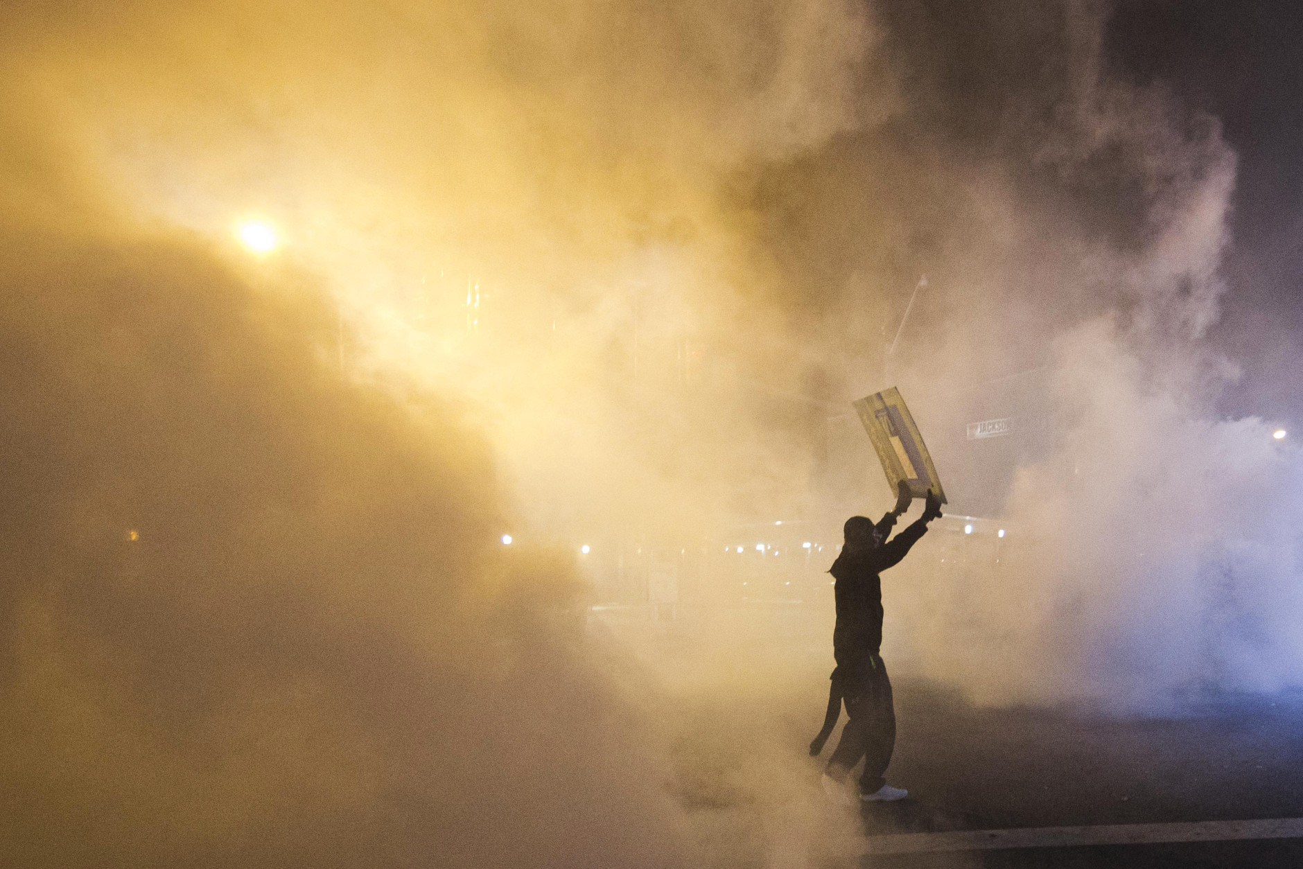 A protestor holds a sign surrounded by smoke Tuesday, April 28, 2015, in Baltimore. A line of police behind riot shields hurled smoke grenades and fired pepper balls at dozens of protesters Tuesday night to enforce a citywide curfew, imposed after the worst outbreak of rioting in Baltimore since 1968. (AP Photo/Matt Rourke)