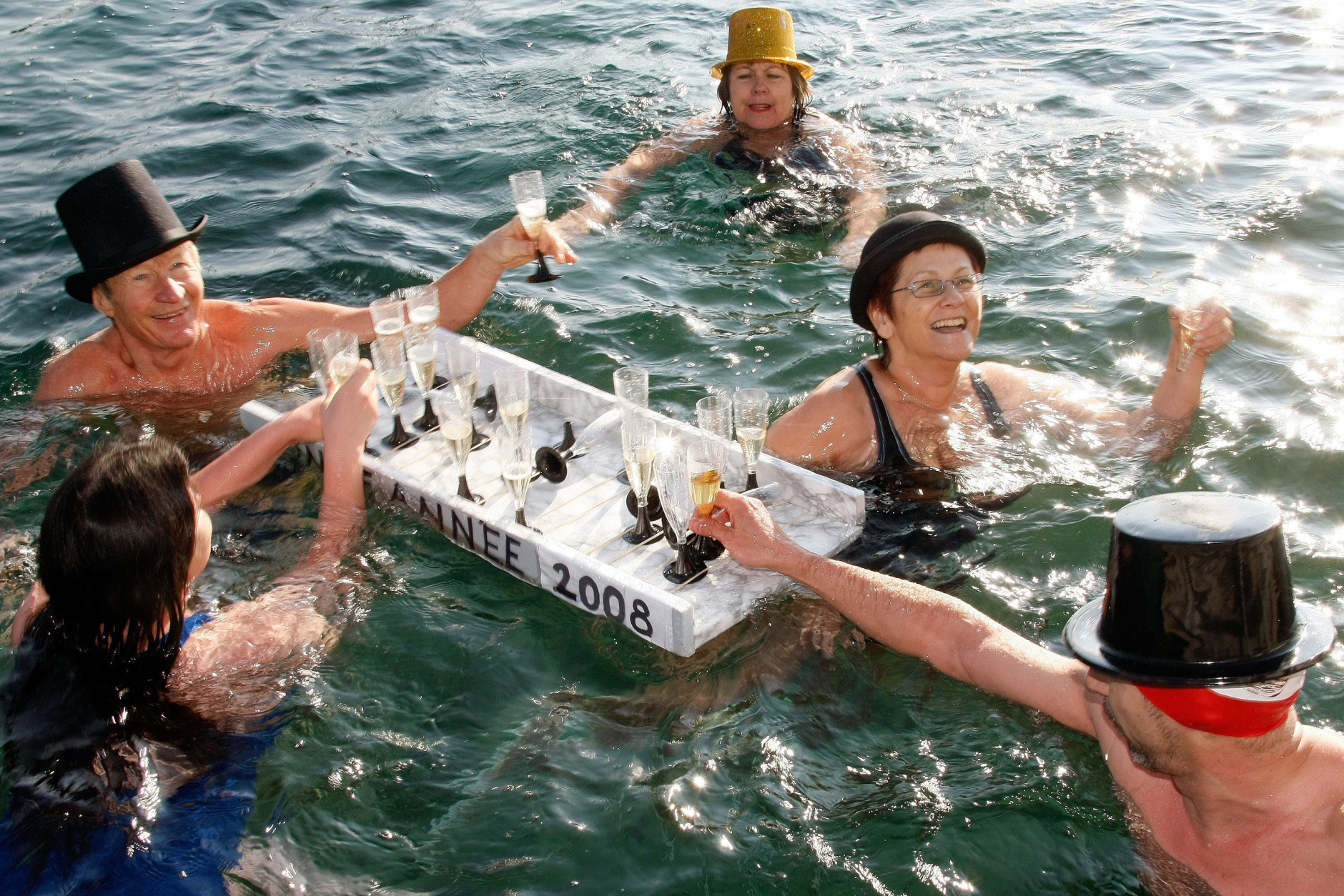 People in fancy costumes carry glasses of champagne while swimming in the chilly water during the annual swim in Lake Geneva, on New Year's day, Tuesday, 1 January 2008. (KEYSTONE/Dominic Favre)