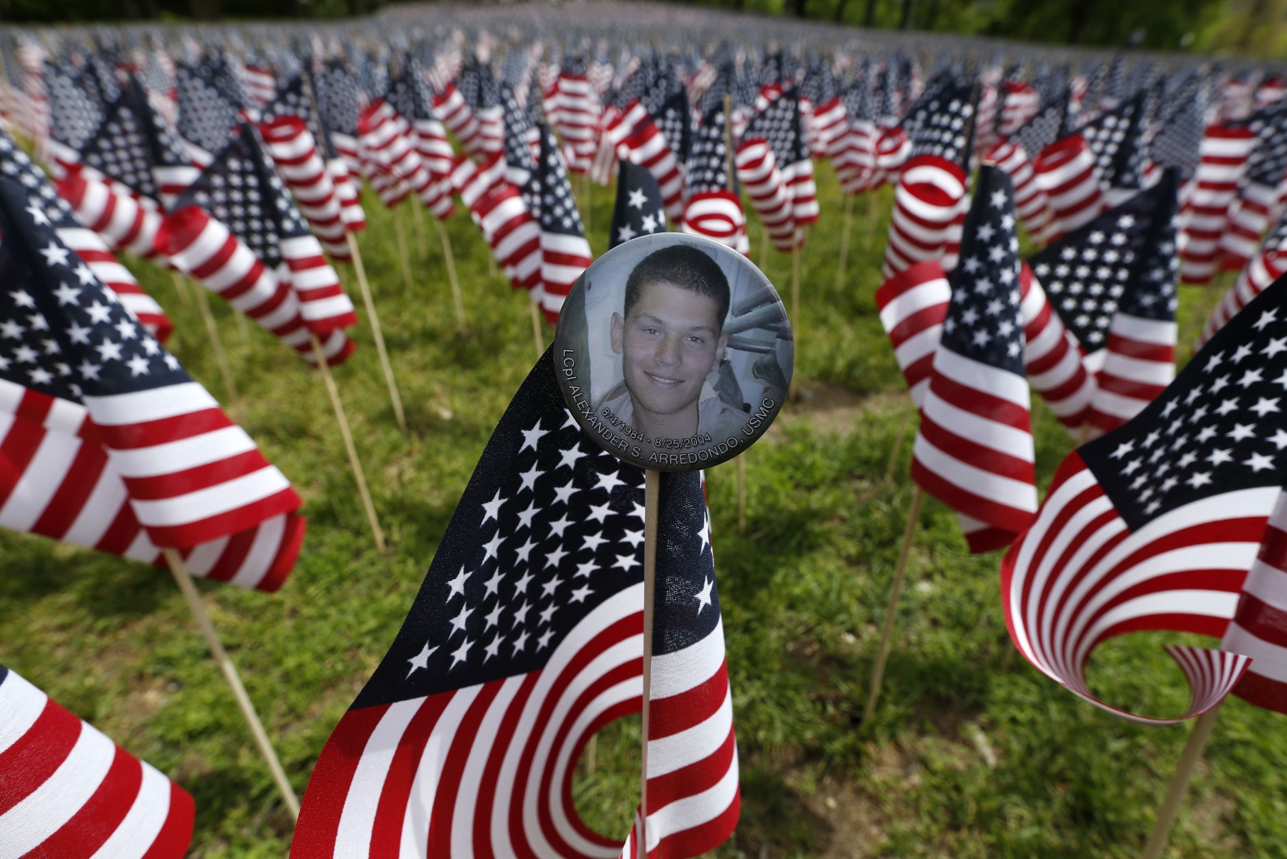 A bbadge with a photograph of Lcpl. Alexander Arredondo is seen attached to a flag in the Massachusetts Military Heroes Fund flag garden on Boston Common in Boston, ahead of Memorial Day, Thursday, May 21 2015. Each of the approximately 37,000 flags represents a Massachusetts military member who died in service from the Revolutionary War to the present. Arredondo is the son of Carlos Arredondo who helped victims at the scene of the Boston Marathon bombings. (AP Photo/Michael Dwyer)