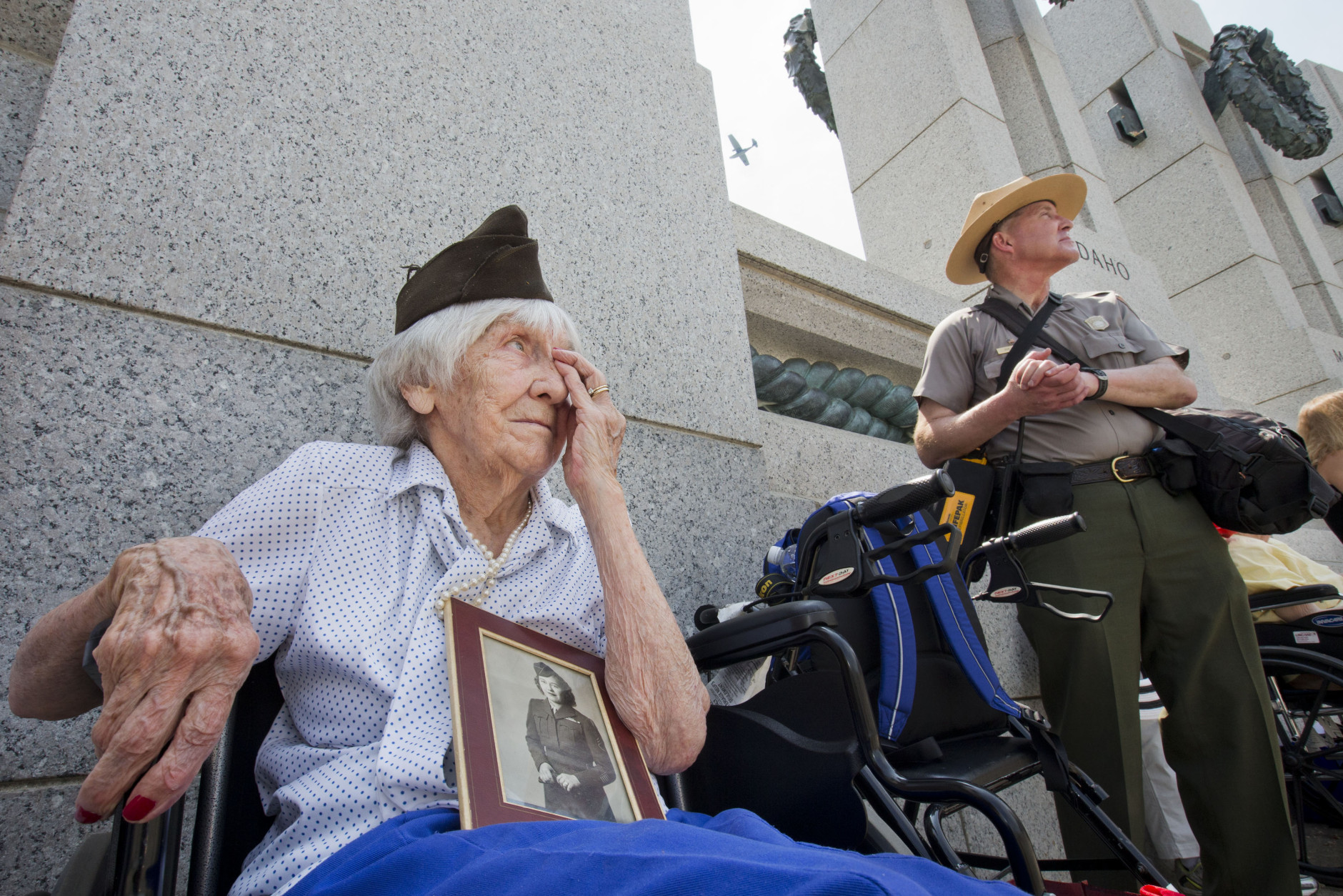 Holding a World War II-era photograph of herself, Elizabeth Copp, 96, of Falls Church, Va., who was a sergeant in the Women's Army Corps during the war, watches as vintage aircraft fly over the World War II Memorial in Washington, Friday, May 8, 2015, in remembrance of the 70th anniversary of Victory in Europe Day (VE Day). The flyover above the National Mall features historically sequenced formations of more than 50 vintage World War II-era aircraft. (AP Photo/Jacquelyn Martin)