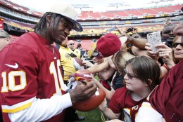 Washington Redskins quarterback Robert Griffin III, left, signs an autograph for a fan during an NFL football draft day fan fest Saturday, May 2, 2015, in Landover, Md. (AP Photo/Alex Brandon)