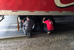 Two men let the air out of the tires of a Coca-Cola truck that is wedged beneath the Memorial Bridge along the George Washington Memorial Parkway Tuesday afternoon.  (WTOP/Jim Battagliese)