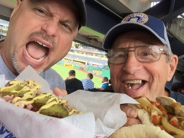 Tom Lohr, left, and his dad enjoy a Cuban at PNC Park in Pittsburgh. The all-beef frank comes with a German pretzel bun and is topped with diced ham, house-smoked pork, mustard and pickles. Lohr ranks the Cuban a 26 for a great specialty dog at a good price. (Courtesy Tom Lohr, The Hot Dog Explorer)