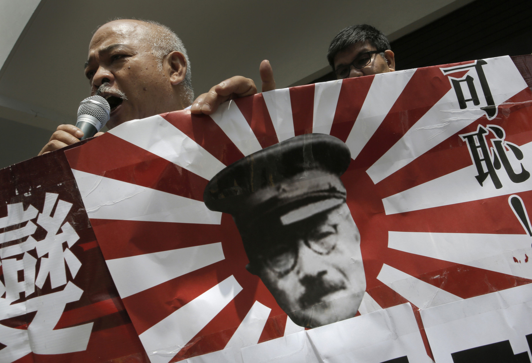 An anti-Japan protester speaks as he holds a Japanese military flag with a cutout picture of Imperial Japanese Army Gen. Hideki Tojo, an executed Class-A war criminal, during a rally near the Japanese Consulate General in Hong Kong, Friday, Sept. 18, 2015, to protest against Japans ruling Liberal Democratic Party that pushed contentious security bills through a legislative committee. The Chinese words on the flag read: " Shame ! " (AP Photo/Vincent Yu)