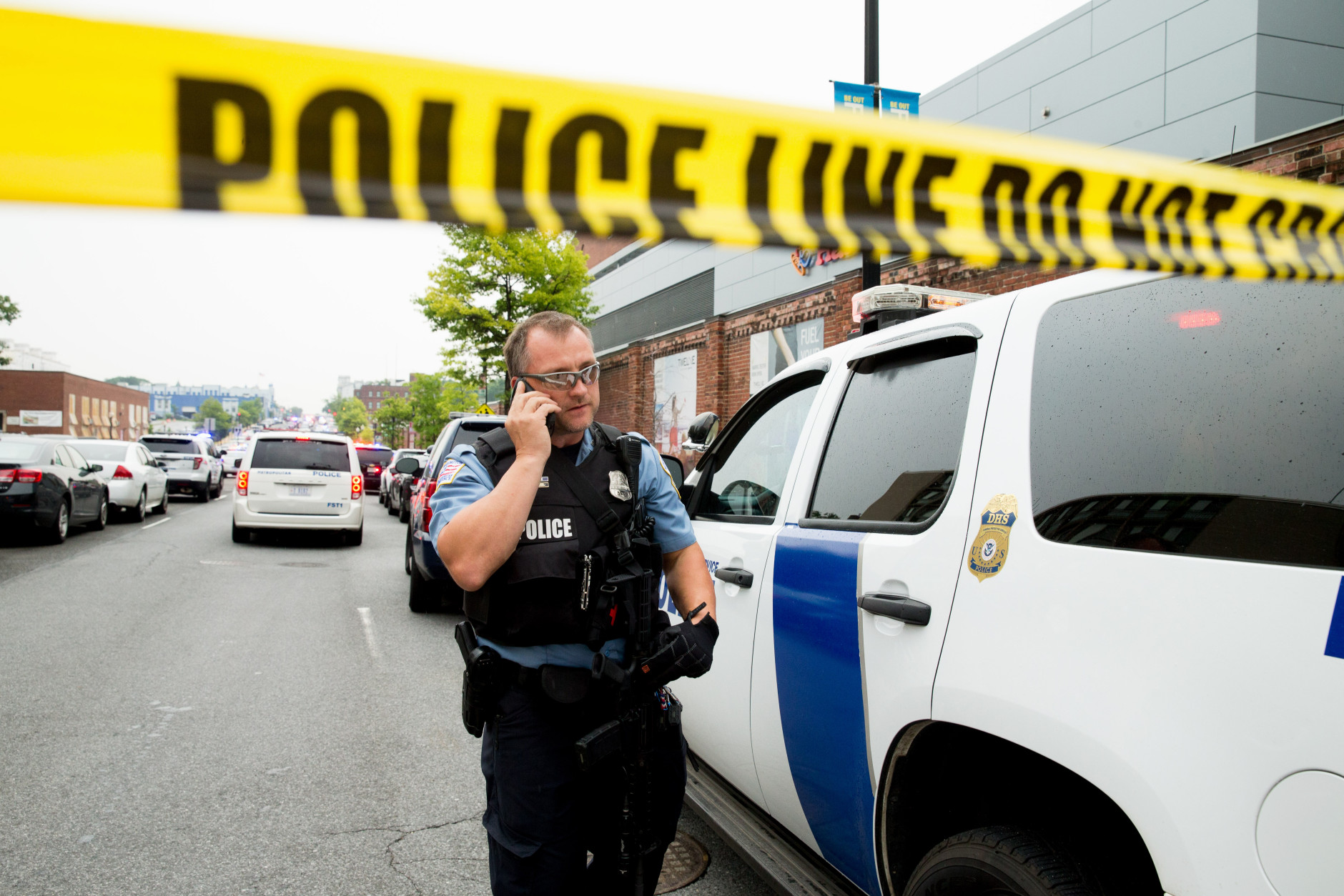 A police officer speaks on his phone as a large police presence gathers along M St. in Southeast Washington, Thursday, July 2, 2015, after an official said shots have been reported in a building on the Washington Navy Yard campus. (AP Photo/Andrew Harnik)