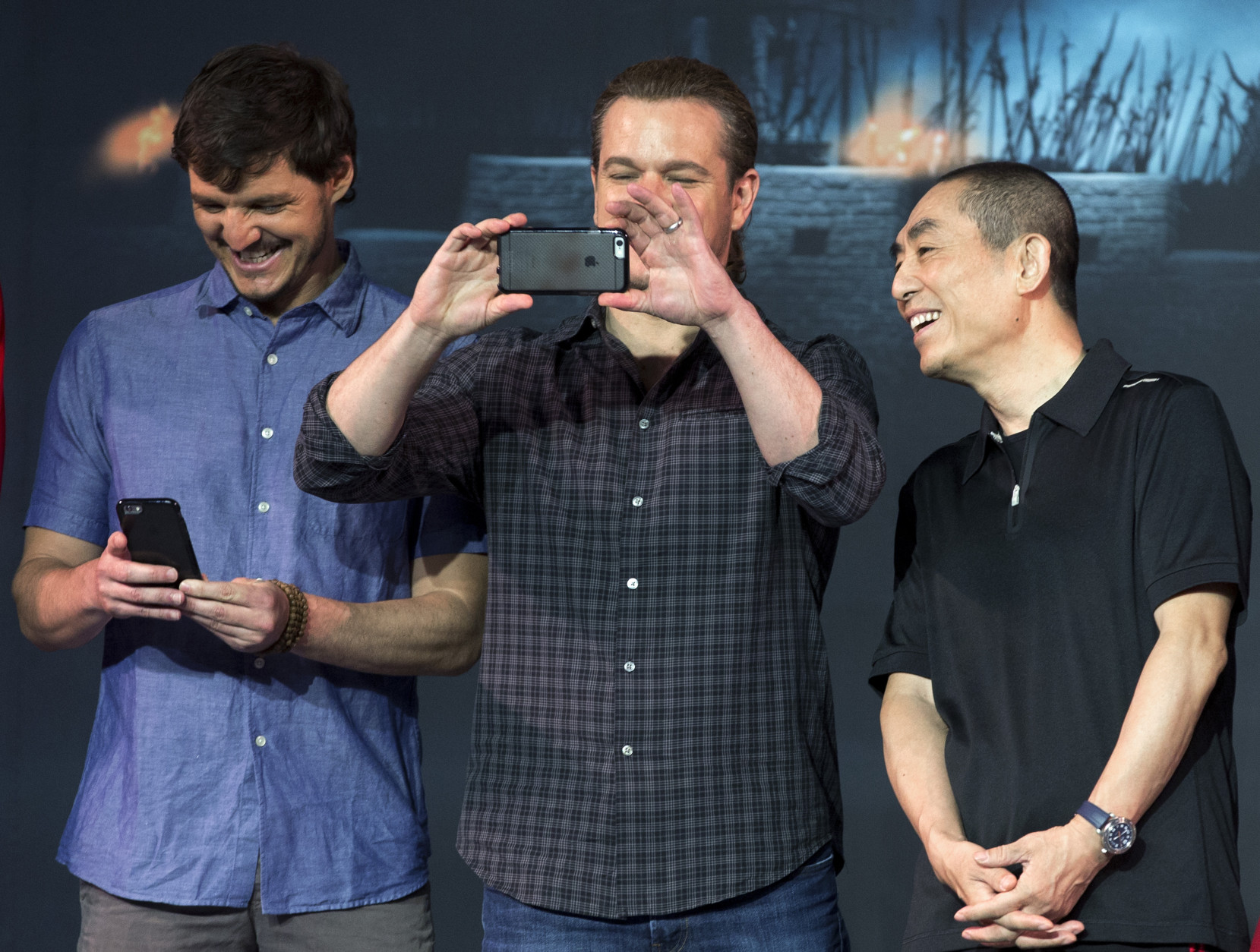 Director Zhang Yimou, right, looks at actor Matt Damon, center, using a mobile phone to take picture of the journalists next to actor Pedro Pascal, second from right, during a press conference for their latest movie The Great Wall held at a hotel in Beijing, China, Thursday, July 2, 2015. (AP Photo/Andy Wong)