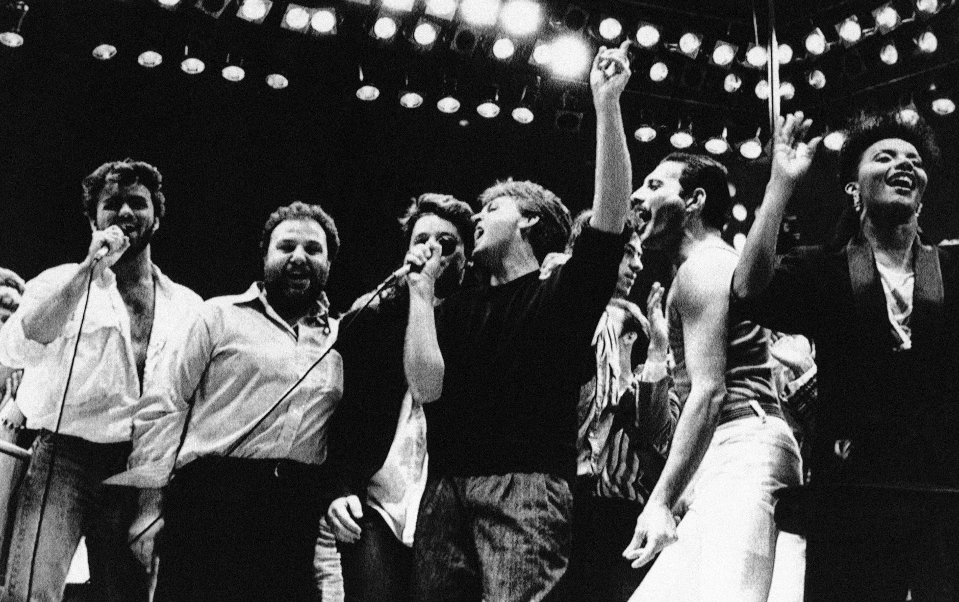Paul McCartney,center with arm raised, joins in the finale of the London Live Aid Famine Relief Concert in London on July 13, 1985. Others, from left, are George Michael of Wham; Harvey Goldsmith, concert promoter; Bono of U2 (face obscured); McCartney; Bob Galdof, organizer; Freddie Mercury of Queen; and unidentified backing singer. (AP Photo/Joe Schaber)