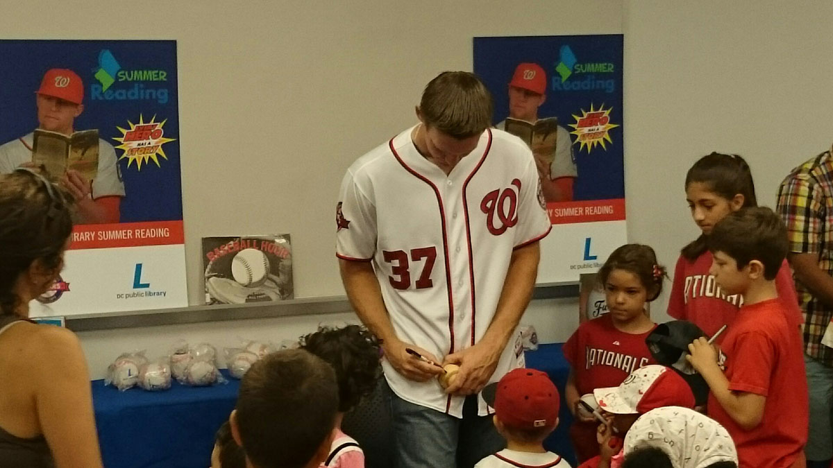Washington Nationals starting pitcher Stephen Strasburg  signs a baseball at  Anacostia Library in Washington, D.C., where he read to young fans on Saturday,  July 18, 2015. ( Dennis J. Foley/WTOP)