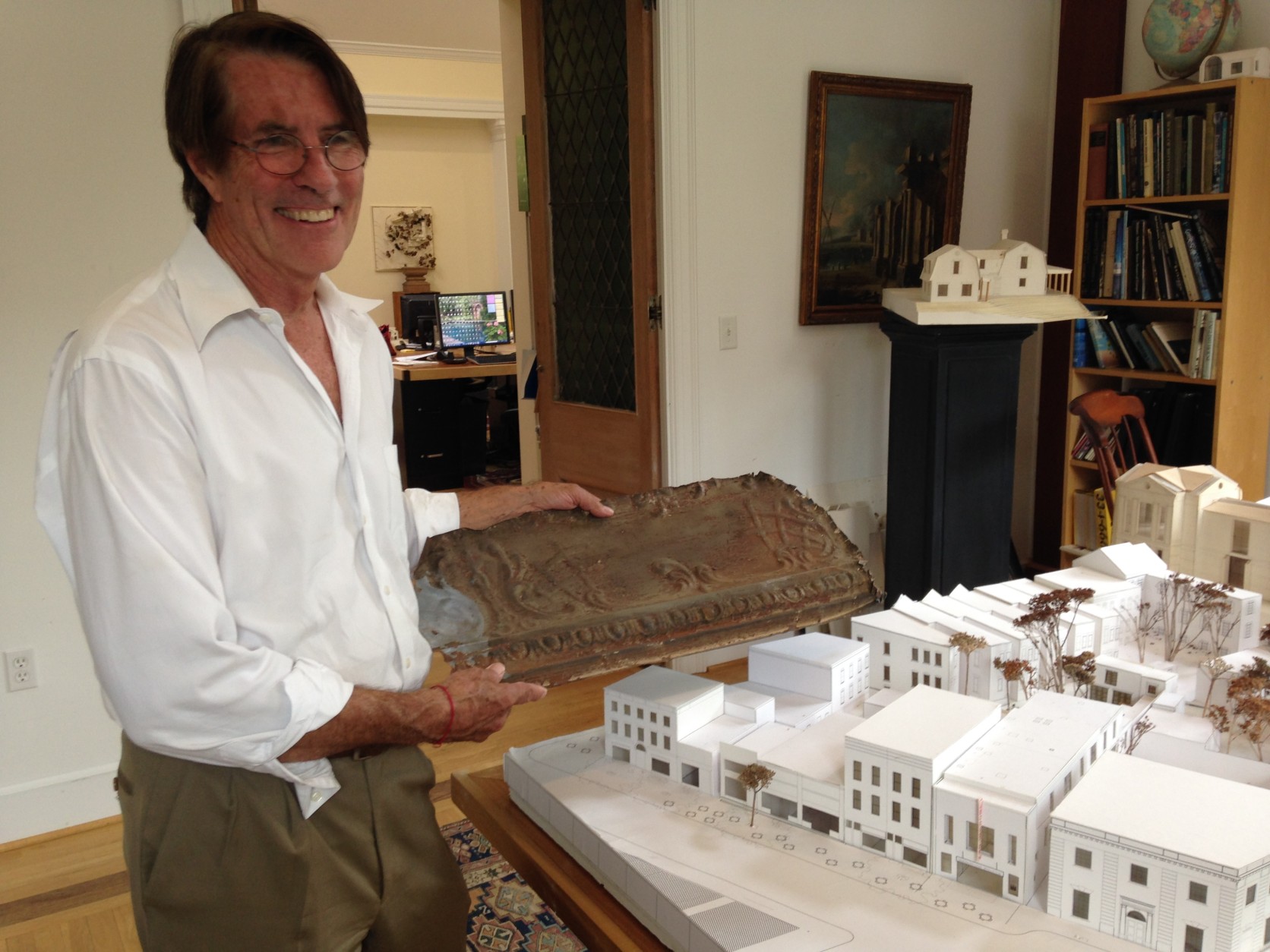 Architect Robert Bell holds a piece of pressed tin cornice from the Georgetown Theater site. It probably dates back to the time when the theater was called the Dumbarton, in the early 1900s. Next to him is a model of the theater and other buildings on the block. (WTOP/Michelle Basch)