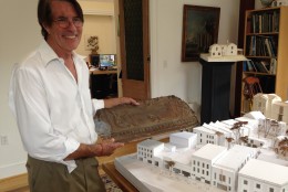 Architect Robert Bell holds a piece of pressed tin cornice from the Georgetown Theater site. It probably dates back to the time when the theater was called the Dumbarton, in the early 1900s. Next to him is a model of the theater and other buildings on the block. (WTOP/Michelle Basch)