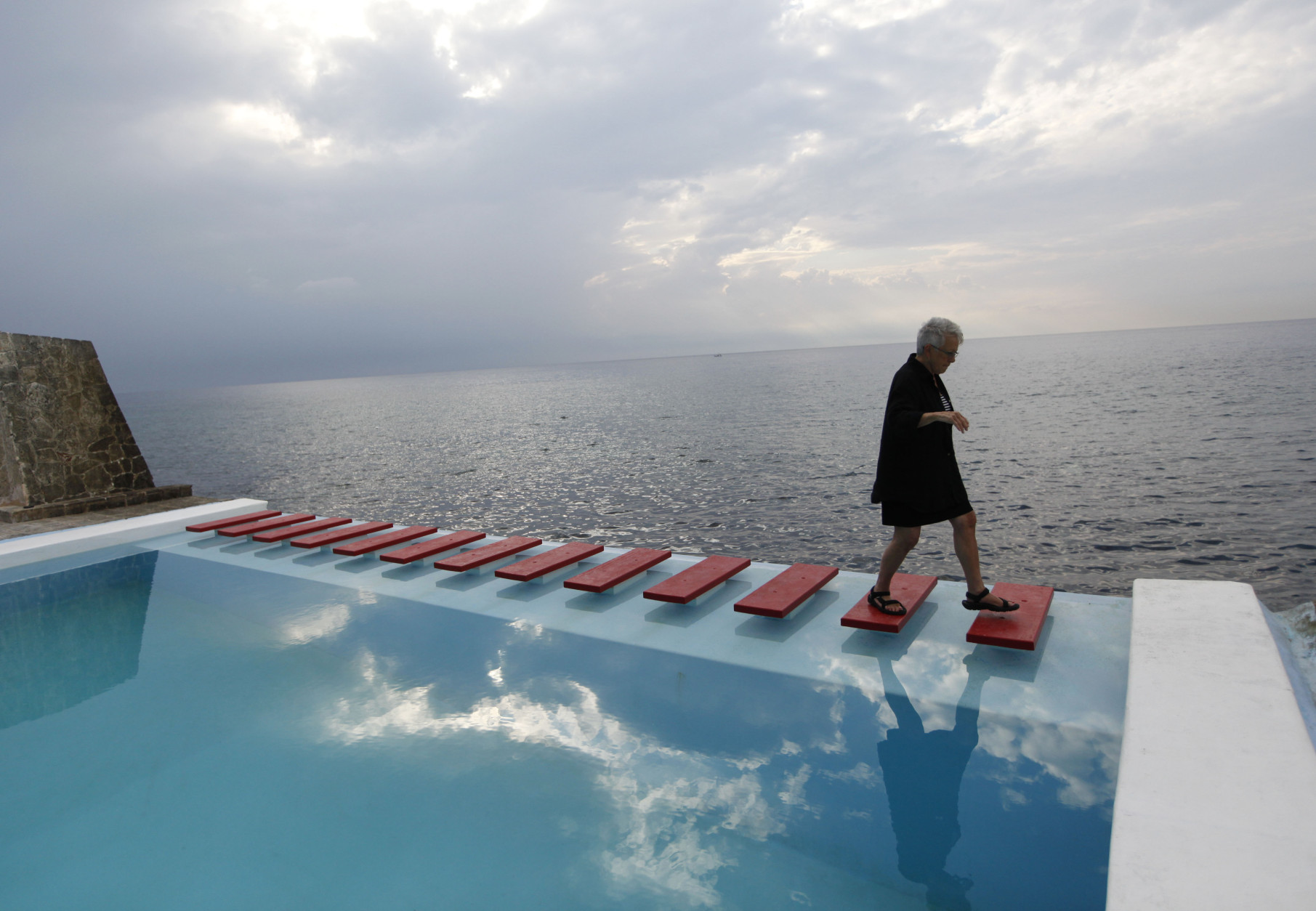 An American tourist walks across the steps of a pool with a view of Havana Bay at Paladar Vistamar in the upscale Miramar section of Havana, Cuba, Thursday, April 19, 2012.  Palardares are privately-run restaurants, usually in private homes, where tourists can dine on higher quality food than the fare generally available in government-run restaurants.(AP Photo/Kathy Willens)