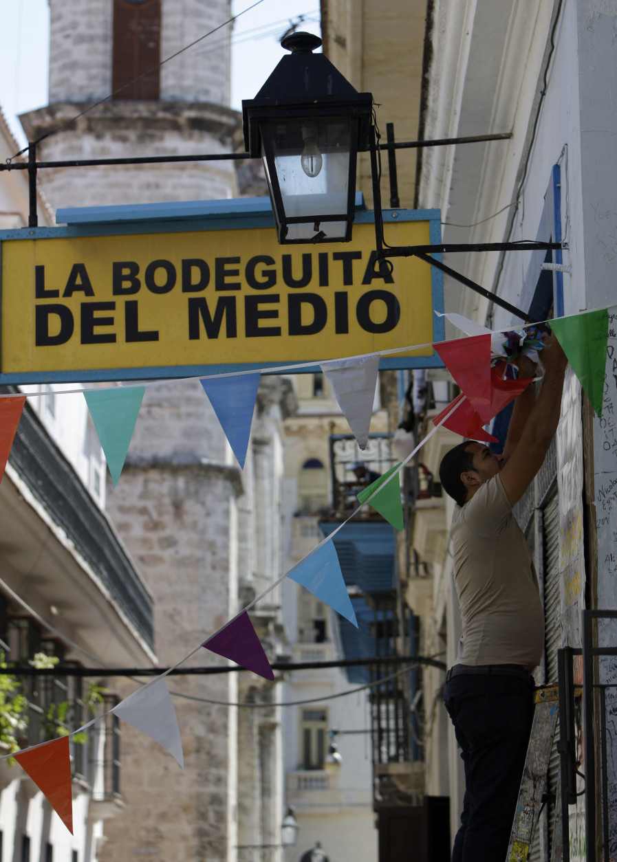 A worker hangs decorative flags outside the famous restaurant-bar "La Bodeguita del Medio" in Old Havana, Cuba, Thursday, April 26, 2012. The restaurant celebrates its 70th anniversary on Thursday. (AP Photo/Franklin Reyes)